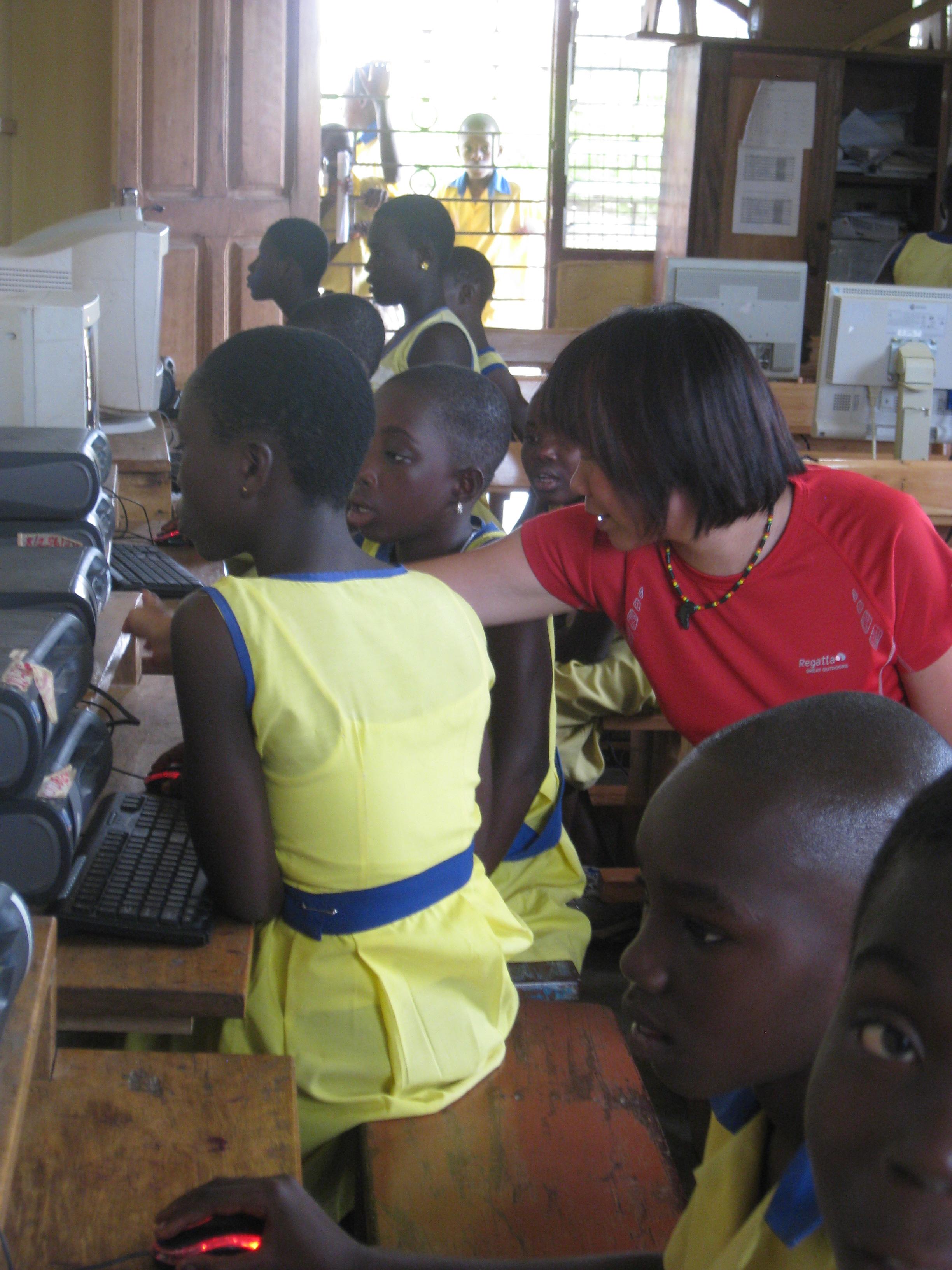 A volunteer teaching IT in Ghana, helps young children on computers during a lesson. A Projects Abroad volunteer gains IT teaching work experience in Ghana by assisting with lessons in the classroom.